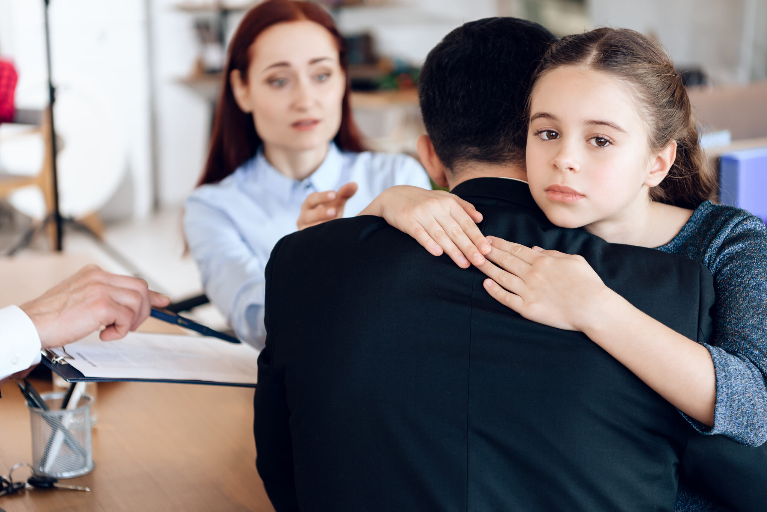 Little girl hugs man in suit sitting opposite woman in lawyer's office.